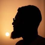 Artistic silhouette of a man in profile against an orange sunset.