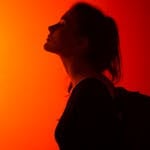 Dramatic silhouette of a woman in profile against a vibrant orange background in a studio setting.