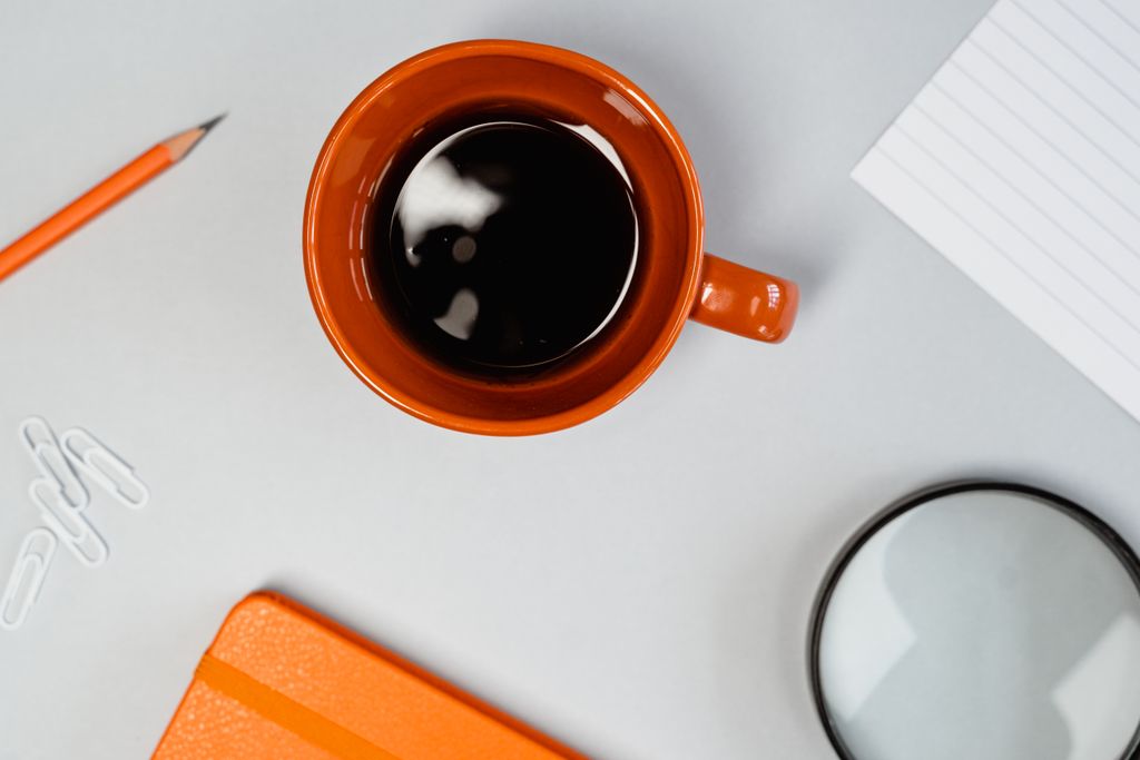 Orange mug with black coffee on a desk with office supplies, a minimal workspace setup.